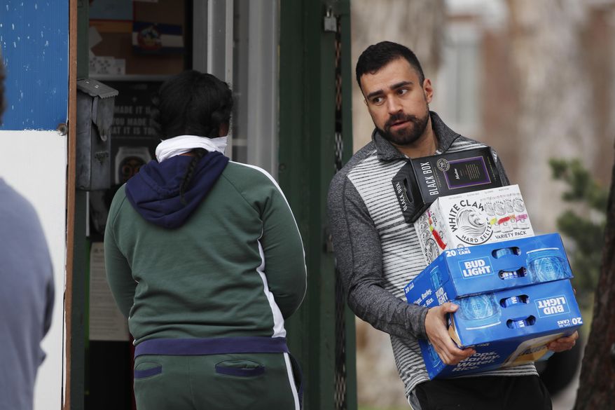 As one shopper enters, another shopper carries his goods out of a liquor store minutes after Denver Mayor Michael Hancock issued a "stay at home" order to reduce the spread of the new coronavirus Monday, March 23, 2020, in Denver. The order, which goes into effect Tuesday, March 24, at 5 p.m., will close all liquor stores, recreational marijuana dispensaries, playgrounds and more through Friday, April 10. According to the World Health Organization, most people recover in about three to six weeks depending on the severity of the COVID-19 illness. (AP Photo/David Zalubowski)