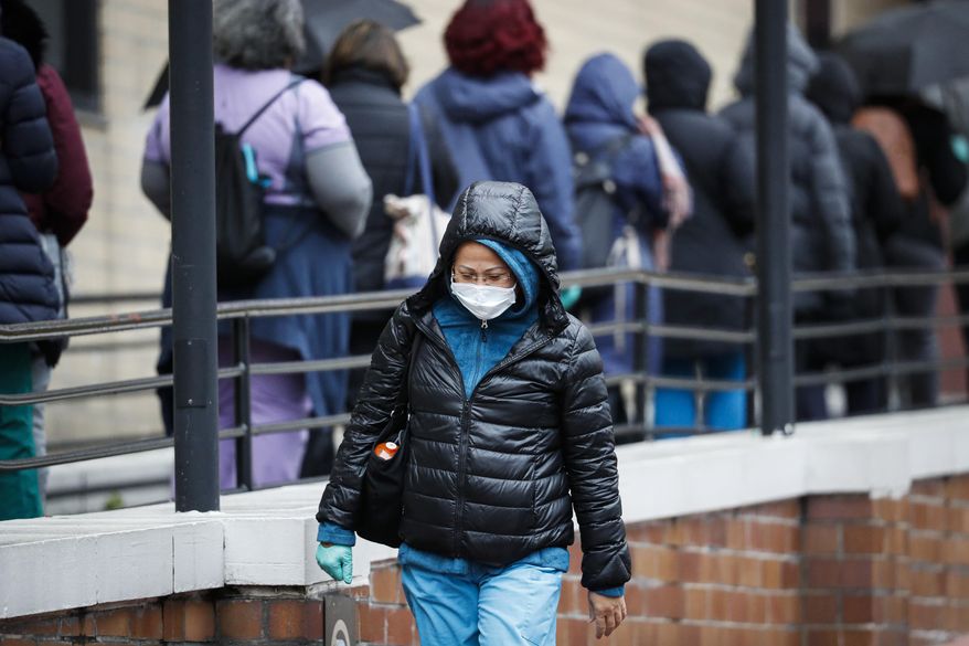 A medical worker wearing a single protective glove and a face mask walks past a line of workers and visitors waiting to be tested for COVID-19, the disease caused by the new coronavirus, at the main entrance to the Department of Veterans Affairs Medical Center, Monday, March 23, 2020, in New York. (AP Photo/John Minchillo) **FILE**