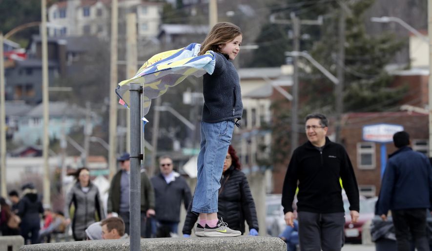 Alexandra Avery, 8, stands atop a beach wall and watches pedestrians pass by before heading out with her family from a busy city park Sunday, March 22, 2020, in Seattle. President Donald Trump on Sunday issued a disaster declaration for Washington and ordered federal assistance for the state, tribal and local response to the coronavirus outbreak that has killed dozens. Health officials reported Sunday that there have been at least 95 coronavirus deaths in Washington state and nearly 2,000 confirmed cases. (AP Photo/Elaine Thompson)