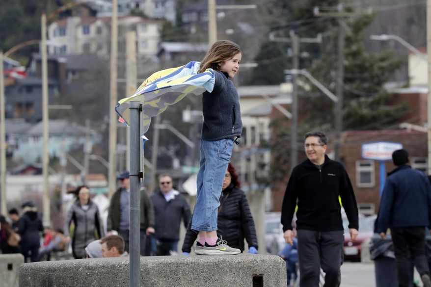 Alexandra Avery, 8, stands atop a beach wall and watches pedestrians pass by before heading out with her family from a busy city park Sunday, March 22, 2020, in Seattle. President Donald Trump on Sunday issued a disaster declaration for Washington and ordered federal assistance for the state, tribal and local response to the coronavirus outbreak that has killed dozens. Health officials reported Sunday that there have been at least 95 coronavirus deaths in Washington state and nearly 2,000 confirmed cases. (AP Photo/Elaine Thompson)