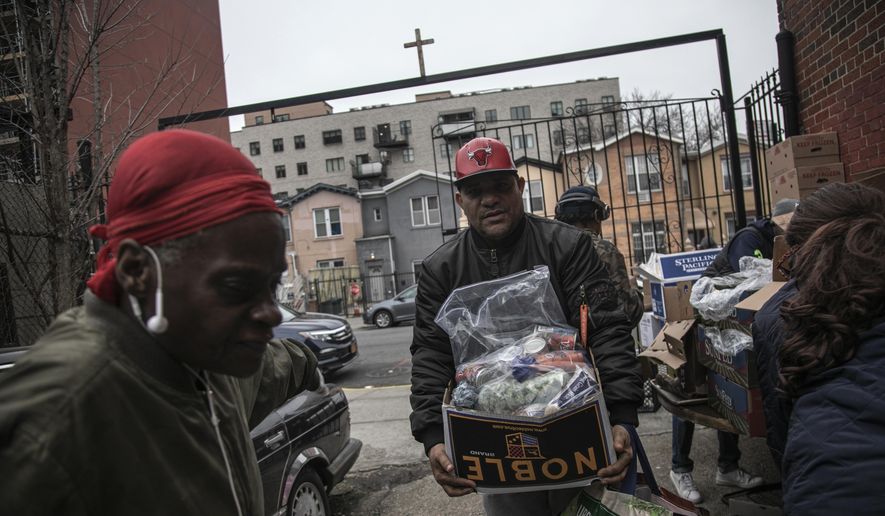 Surrounded by a few volunteers, a man carries food donations from St. Stephen Outreach in the Brooklyn borough of New York, on Friday, March 20, 2020. (AP Photo/Wong Maye-E)