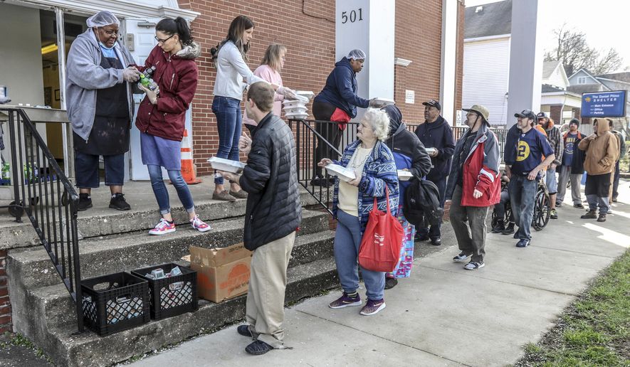 A line forms at the front steps of the Daniel Pitino Shelter as shelter staff serve carry out lunch meals to visitors, Wednesday, March 25, 2020, in Owensboro, Ky. Lunch is normally served in the shelter&#x27;s dining area but carry out is now the current protocol for the shelter during the coronavirus pandemic. (Greg Eans/The Messenger-Inquirer via AP)