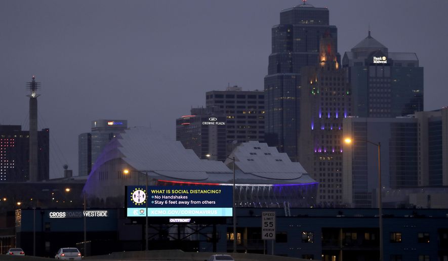 A sign about social distancing stands against the downtown skyline Tuesday, March 24, 2020 on the first day of a stay-at-home order in Kansas City, Mo. Kansas City and surrounding counties instituted a 30-day mandatory stay-at-home order in an effort to stem the spread of the coronavirus. (AP Photo/Charlie Riedel)