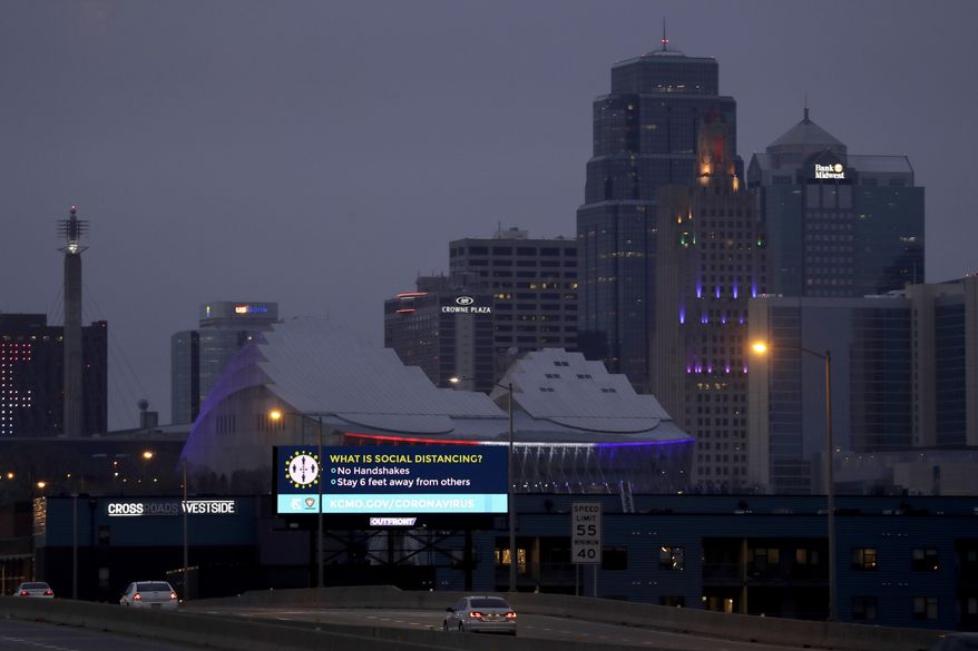 A sign about social distancing stands against the downtown skyline Tuesday, March 24, 2020 on the first day of a stay-at-home order in Kansas City, Mo. Kansas City and surrounding counties instituted a 30-day mandatory stay-at-home order in an effort to stem the spread of the coronavirus. (AP Photo/Charlie Riedel)