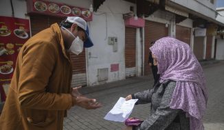 A member of security forces inspects a permit allowing a woman to leave her home, after a health state of emergency was declared and members of the public ordered to a home confinement, in Rabat, Morocco, Sunday, March 22, 2020. For some people the COVID-19 coronavirus causes mild or moderate symptoms, but for some it can cause severe illness including pneumonia.(AP Photo/Mosa&#39;ab Elshamy)