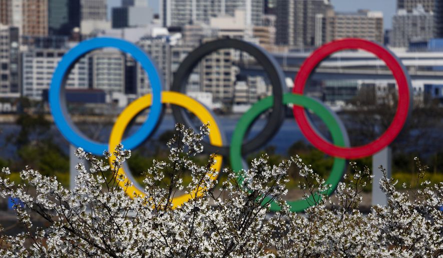 The Olympic rings are seen behind cherry blossoms Wednesday, March 25, 2020, in the Odaiba section of Tokyo. Not even the Summer Olympics could withstand the force of the coronavirus. After weeks of hedging, the IOC took the unprecedented step of postponing the world's biggest sporting event, a global extravaganza that's been cemented into the calendar for more than a century. (AP Photo/Jae C. Hong) **FILE**