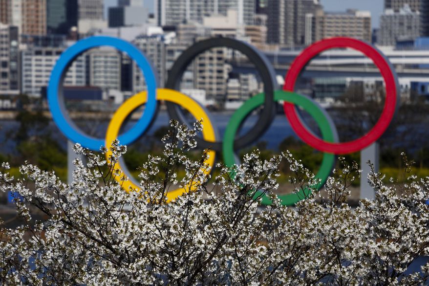 The Olympic rings are seen behind cherry blossoms Wednesday, March 25, 2020, in the Odaiba section of Tokyo. Not even the Summer Olympics could withstand the force of the coronavirus. After weeks of hedging, the IOC took the unprecedented step of postponing the world's biggest sporting event, a global extravaganza that's been cemented into the calendar for more than a century. (AP Photo/Jae C. Hong) **FILE**
