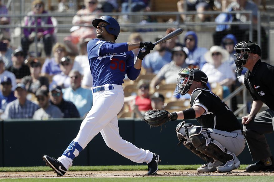 Los Angeles Dodgers' Mookie Betts, left, flies out as Chicago White Sox catcher Zack Collins, right, looks on during the first inning of a spring training baseball game Monday, Feb. 24, 2020, in Glendale, Ariz. (AP Photo/Gregory Bull)