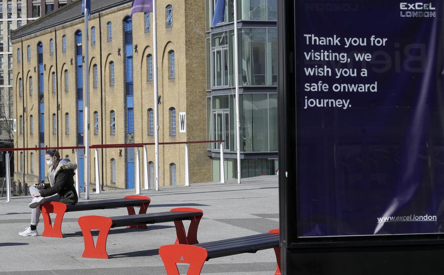 A woman wearing a protective mask sits outside the ExCel centre in London, Wednesday, March 25, 2020. The British Government announced Tuesday, that the ExCel Center in east london will become a 4,000 bed temporary hospital to deal with future coronavirus patients, to be called NHS Nightingale. The new coronavirus causes mild or moderate symptoms for most people, but for some, especially older adults and people with existing health problems, it can cause more severe illness or death.(AP Photo/Kirsty Wigglesworth)