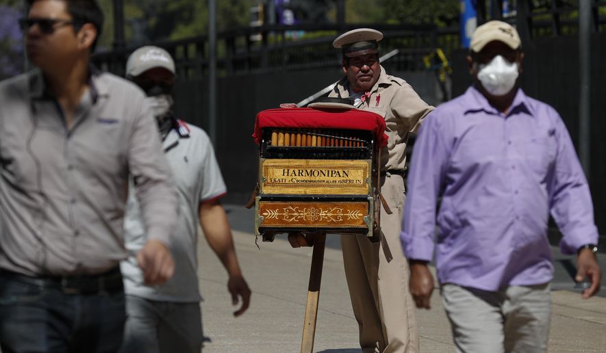 Organ grinder Moises Rosas solicits tips from pedestrians in central Mexico City, Tuesday, March 24, 2020. Rosas, who has been an organ grinder for 25 years, says he isn't afraid of the new coronavirus and needs the average of 200 pesos (around $8.50) he takes home per day. "We live from day to day, so if we don't work, there won't be income for the house, the family." (AP Photo/Rebecca Blackwell)