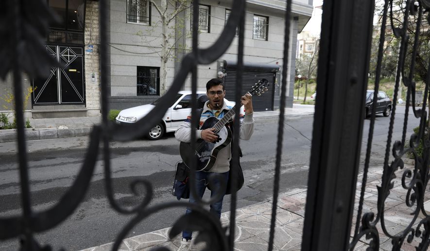 A street musician sings and plays music on an empty lane in Tehran, Iran, Thursday, March 26, 2020. Iran is battling the worst new coronavirus outbreak in the region and authorities have advised people to stay at home and trying to enforce new policy imposing the kinds of lockdowns when the country spending the new year holidays. (AP Photo/Vahid Salemi)