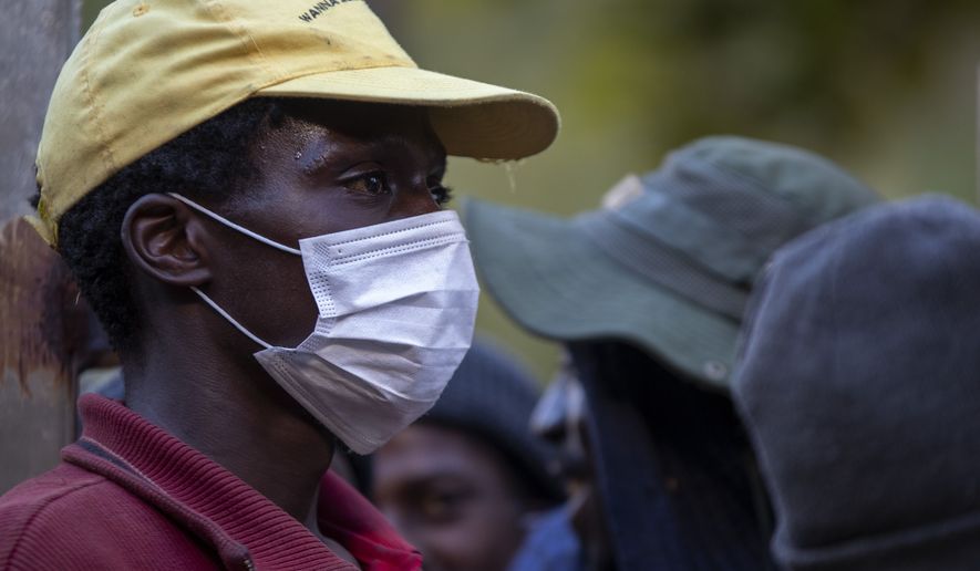 A man wearing face masks to protect herself against coronavirus, mends the gate as homeless people are queuing for a meal and a shelter in Hillbrow, Johannesburg, South Africa, Friday, March 27, 2020. South Africa went into a nationwide lockdown for 21 days in an effort to mitigate the spread to the coronavirus.  (AP Photo/Themba Hadebe)