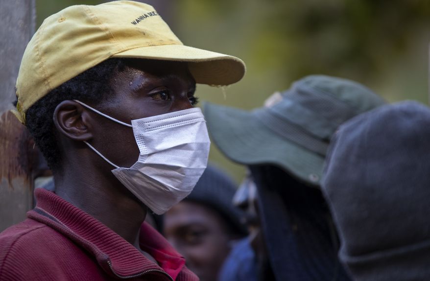 A man wearing face masks to protect herself against coronavirus, mends the gate as homeless people are queuing for a meal and a shelter in Hillbrow, Johannesburg, South Africa, Friday, March 27, 2020. South Africa went into a nationwide lockdown for 21 days in an effort to mitigate the spread to the coronavirus.  (AP Photo/Themba Hadebe)