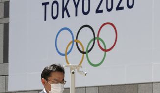 FILE - In this Wednesday, March 25, 2020, file photo, a masked man walks in front of a Tokyo Olympics logo at the Tokyo metropolitan government headquarters building in Tokyo. The Tokyo Olympics have been moved to next year. But countless questions remain. They revolve around 11,000 Olympic athletes and 4,400 Paralympic athletes. They also include 206 national Olympic committees, sports federations, thousands of contracts, and billions of dollars. (AP Photo/Koji Sasahara, File)