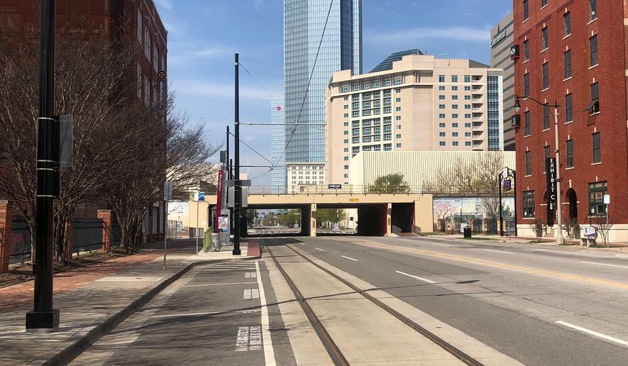 The Devon Energy Center, the tallest building in Oklahoma, towers over empty parking spaces and a barren Sheridan Avenue where businesses are largely closed in the normally vibrant Bricktown section of Oklahoma City, Friday, March 27, 2020. (AP Photo/Cliff Brunt)