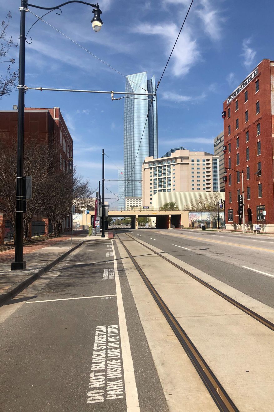 The Devon Energy Center, the tallest building in Oklahoma, towers over empty parking spaces and a barren Sheridan Avenue where businesses are largely closed in the normally vibrant Bricktown section of Oklahoma City, Friday, March 27, 2020. (AP Photo/Cliff Brunt)