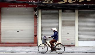 A woman cycles past closed shops in Hanoi, Vietnam, Friday, March 27, 2020. Vietnam&#39;s Prime Minister Nguyen Xuan Phuc has ordered to shut down non-essential business to curb the spread of COVID-19. The new coronavirus causes mild or moderate symptoms for most people, but for some, especially older adults and people with existing health problems, it can cause more severe illness or death. (AP Photo/Hau Dinh)