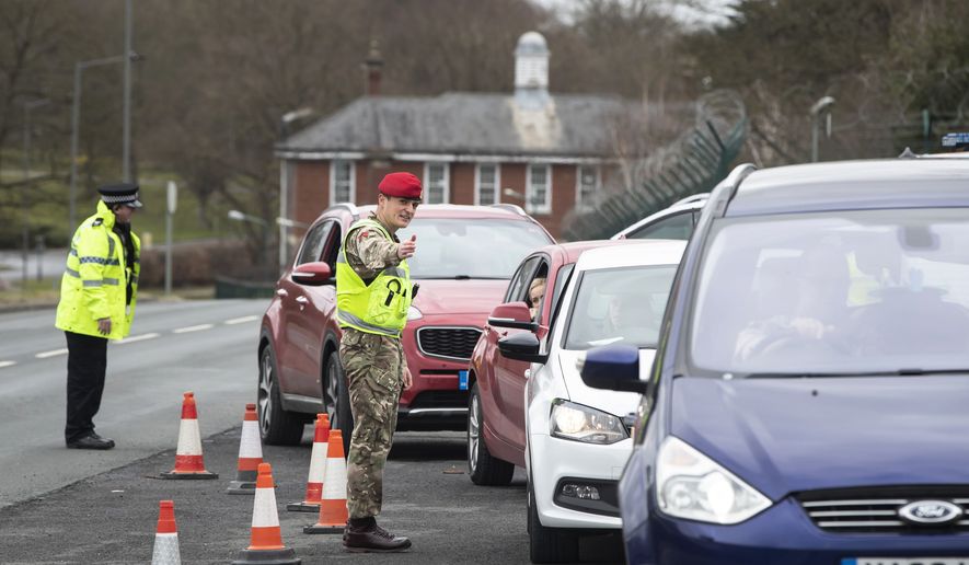 A member of the Royal Military Police works alongside local police, to monitor motorists at a vehicle checkpoint to ensure people are complying with government restrictions to only make essential journeys, in Catterick, north England, Saturday, March 28, 2020. (Danny Lawson / PA via AP)