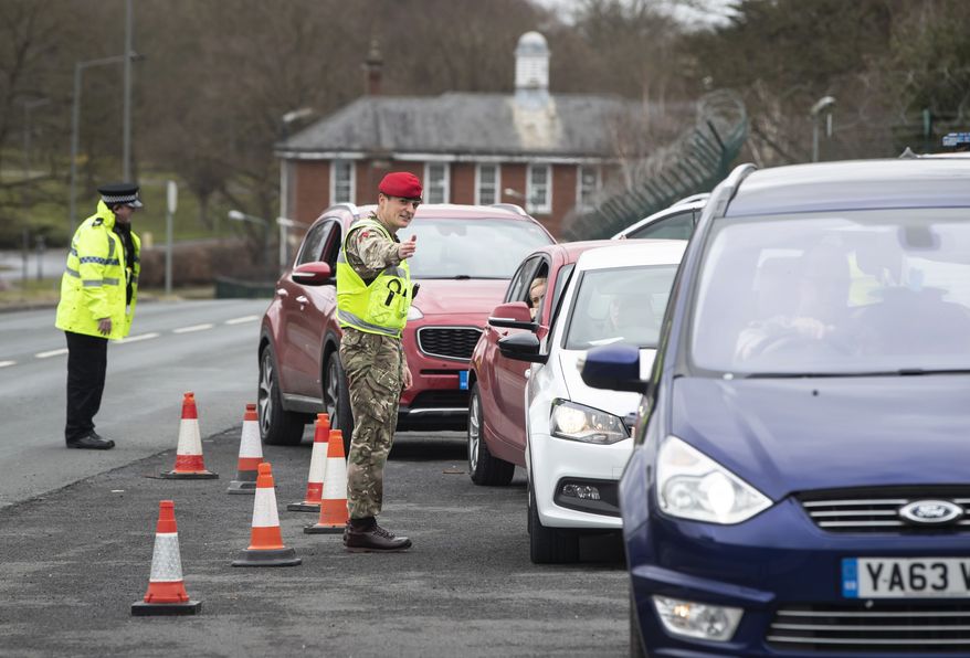 A member of the Royal Military Police works alongside local police, to monitor motorists at a vehicle checkpoint to ensure people are complying with government restrictions to only make essential journeys, in Catterick, north England, Saturday, March 28, 2020. (Danny Lawson / PA via AP)
