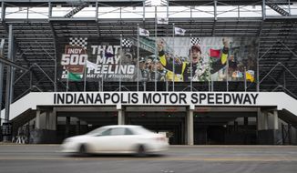 A car drives past the entrance at the Indianapolis Motor Speedway in Indianapolis, Saturday, March 28, 2020. Roger Penske, at 83 and considered high risk to the coronavirus as a 2017 kidney transplant recipient, still makes the daily three-minute commute to his Bloomfield Hills, Mich, office. He works 12 or more hours a day from his conference room at Penske Corp., which has a skeleton crew all practicing social distancing. Penske also had the small matter of planning his first Indianapolis 500. (AP Photo/Michael Conroy)