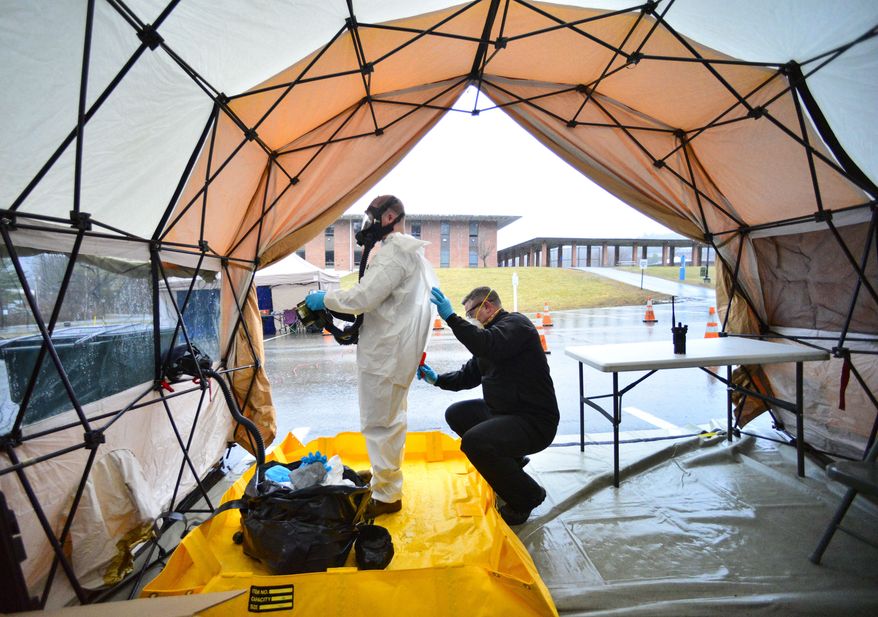 Sgt. First Class Mason Lord, with the Vermont Army National Guard, helps remove a personal protective equipment suit in a decontamination zone at the COVID-19 testing facility in a parking lot of Landmark College, in Putney, Vt., &amp;#160;that was set up to test people with mild to moderate symptoms of the virus on Sunday, March 29, 2020. (Kristopher Radder/Brattleboro Reformer via AP)