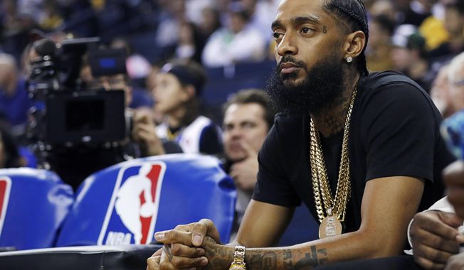 FILE - In this March 29, 2018, file photo, rapper Nipsey Hussle watches an NBA basketball game between the Golden State Warriors and the Milwaukee Bucks in Oakland, Calif. Hussle, 33, was shot and killed outside his Los Angeles clothing store on March 31, 2019. A year after Hussle&#x27;s death, his popularity and influence are as strong as ever. He won two posthumous Grammys in January, he remains a favorite of his hip-hop peers and his death has reshaped his hometown of Los Angeles in some unexpected ways. (AP Photo/Marcio Jose Sanchez, File)