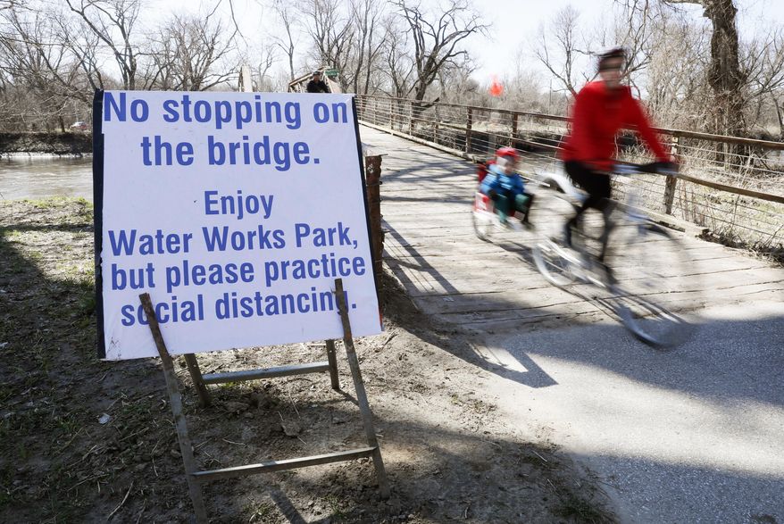 A cyclist passes a sign directing riders to practice social distancing on a bridge in Water Works Park, Monday, March 30, 2020, in Des Moines, Iowa. The new coronavirus causes mild or moderate symptoms for most people, but for some, especially older adults and people with existing health problems, it can cause more severe illness or death. (AP Photo/Charlie Neibergall)