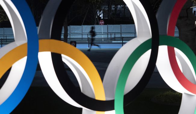 A man jogs past the Olympic rings Monday, March 30, 2020, in Tokyo. The Tokyo Olympics will open next year in the same time slot scheduled for this year&#x27;s games. Tokyo organizers said Monday the opening ceremony will take place on July 23, 2021. (AP Photo/Jae C. Hong)
