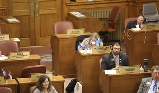 In this photo provided by Patrick Callahan, several House lawmakers sit at their desks on the House floor while they debated and voted through a teleconference system Monday March 30, 2020, in Pierre, S.D.. Rep. Julie Frye-Mueller, a Rapid City Republican, wore a mask and gloves due to the coronavirus pandemic. They were considering emergency bills pushed by Gov. Kristi Noem. (Patrick Callahan/South Dakota Broadcasters Association via AP)