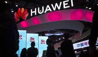 In this Oct. 31, 2019, file photo, attendees walk past a display for 5G services from Chinese technology firm Huawei at the PT Expo in Beijing. (AP Photo/Mark Schiefelbein, File)