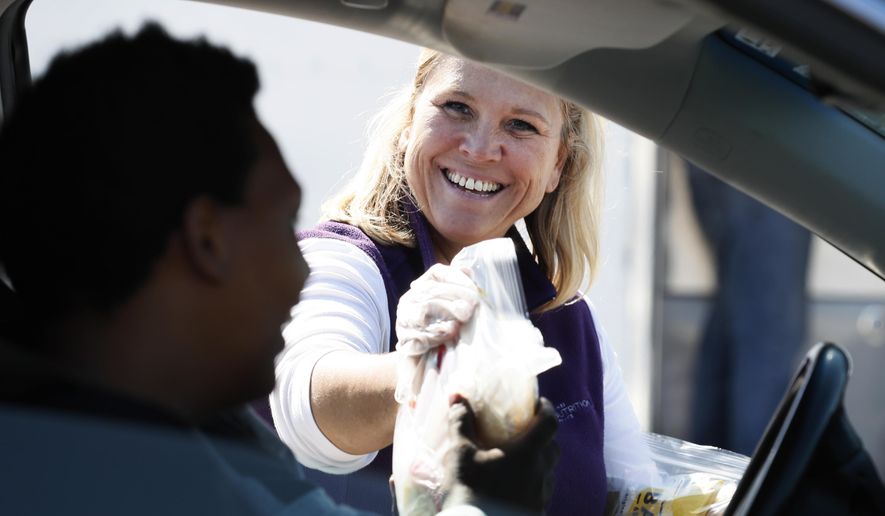 Waukee Community Schools Nutrition Services Department employee Billie Veach hands out free grab-and-go meals for children under eighteen years of age in response to the coronavirus outbreak, Tuesday, March 31, 2020, in Waukee, Iowa. The new coronavirus causes mild or moderate symptoms for most people, but for some, especially older adults and people with existing health problems, it can cause more severe illness or death. (AP Photo/Charlie Neibergall)