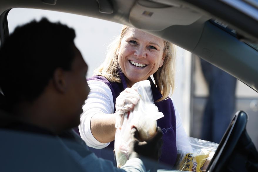 Waukee Community Schools Nutrition Services Department employee Billie Veach hands out free grab-and-go meals for children under eighteen years of age in response to the coronavirus outbreak, Tuesday, March 31, 2020, in Waukee, Iowa. The new coronavirus causes mild or moderate symptoms for most people, but for some, especially older adults and people with existing health problems, it can cause more severe illness or death. (AP Photo/Charlie Neibergall)