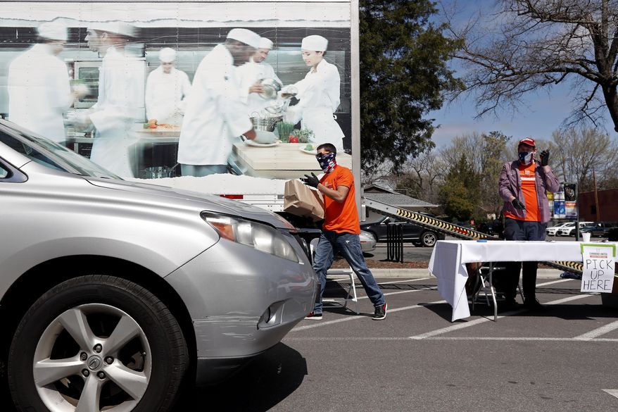 Randy Barnes, a worker for Carrboro United that is providing local restaurants and farmers a way to sell their food, takes a bag filled with locally sourced food items to a waiting customer at a pickup location in Carrboro, N.C., Thursday, March 26, 2020. The food hub is run by restaurant workers who have been laid off due to the COVID-19 coronavirus. (AP Photo/Gerry Broome)