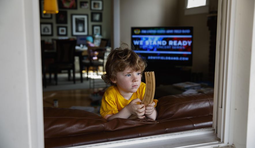 Ethan McIver, 4, son of U.S. Army Field Band member Sgt. Major Robert McIver, Jr., holds part of his toy train set as he looks out the window of his home in Catonsville, Md., Thursday, March 26, 2020. The family is staying home because of the coronavirus outbreak. Inside on the television the U.S. Army Field Band's daily "We Stand Ready" virtual concert series from Fort George G. Meade is playing. The Army Field Band's mission is to bring the military's story to the American people. And they're not letting the coronavirus get in the way. (AP Photo/Carolyn Kaster)