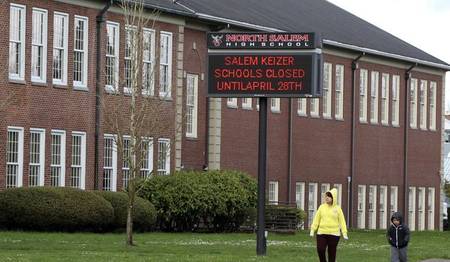 A woman and child walk past North Salem High School on Tuesday, March 31, 2020, which like all schools in Oregon, is closed until April 28, 2020, because of the coronavirus. Facing an expected closure through the end of the academic year, schools across Oregon have been told to begin distance learning on April 13, 2020. (AP Photo/Andrew Selsky)  **FILE**