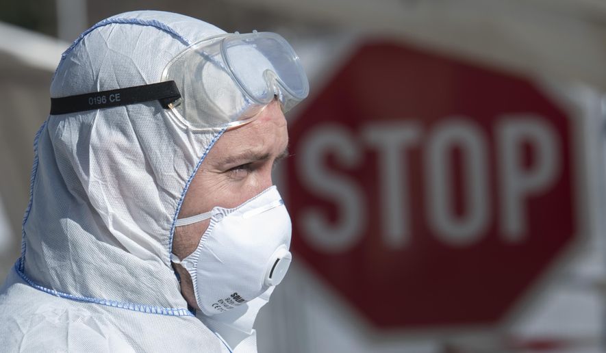 Corporal Mathias Jahn, left, member of the German armed forces Bundeswehr, stands in front of a mobile coronavirus test station and demonstrates his work in a test run after a press conference at a drive-through (drive-in) COVID-19 testing center in Gera, Germany, Wednesday, April 1, 2020. The appointment-only drive-through testing center began twelfe days ago. Medical staff reach into a car to take a nasopharyngeal swab from a patient. For most people, the new coronavirus causes only mild or moderate symptoms, such as fever and cough. For some, especially older adults and people with existing health problems, it can cause more severe illness, including pneumonia. (AP Photo/Jens Meyer)