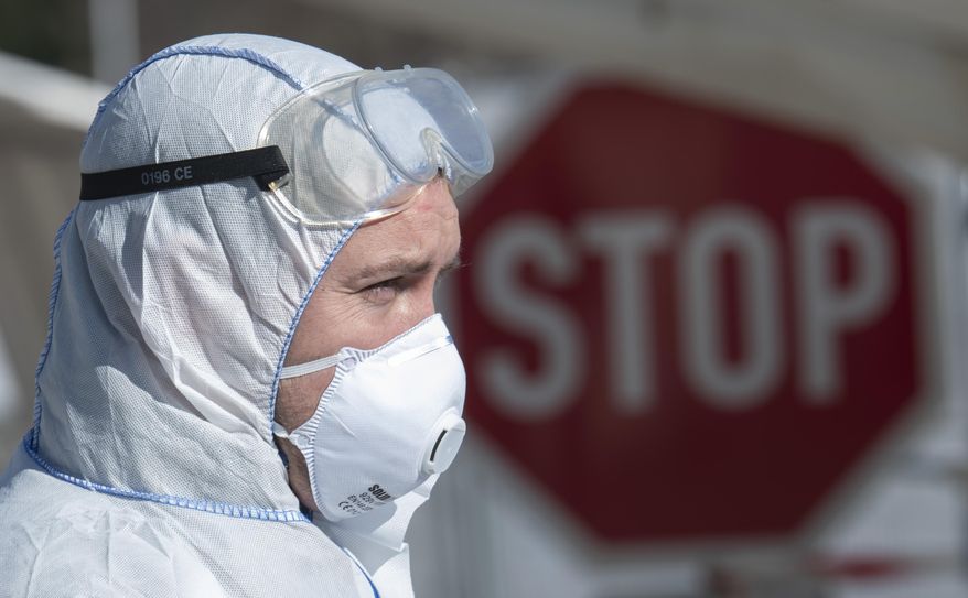 Corporal Mathias Jahn, left, member of the German armed forces Bundeswehr, stands in front of a mobile coronavirus test station and demonstrates his work in a test run after a press conference at a drive-through (drive-in) COVID-19 testing center in Gera, Germany, Wednesday, April 1, 2020. The appointment-only drive-through testing center began twelfe days ago. Medical staff reach into a car to take a nasopharyngeal swab from a patient. For most people, the new coronavirus causes only mild or moderate symptoms, such as fever and cough. For some, especially older adults and people with existing health problems, it can cause more severe illness, including pneumonia. (AP Photo/Jens Meyer)