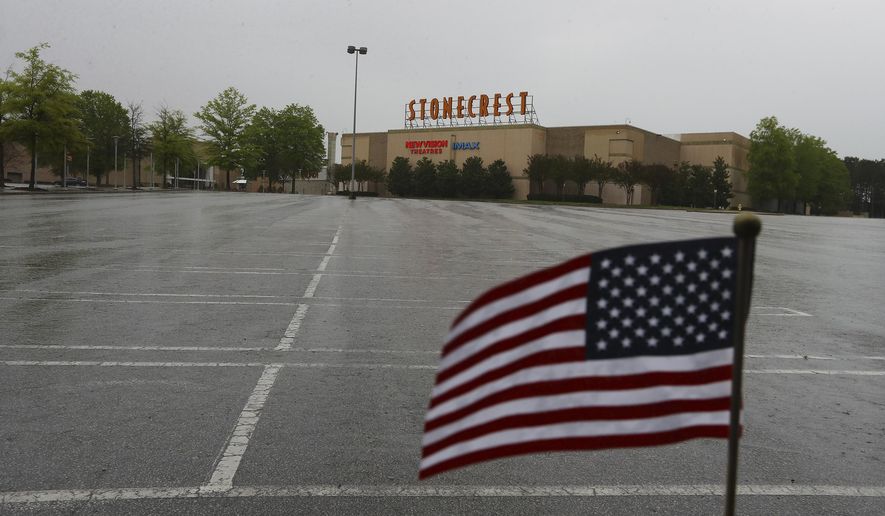 A small U.S. flag flutters at the edge of an empty parking lot outside The Mall at Stonecrest and New Vision Theatres, closed during the coronavirus pandemic, Tuesday, March 31, 2020, in Stonecrest, Ga. (Curtis Compton/Atlanta Journal-Constitution via AP)