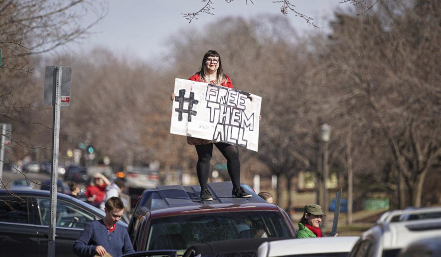 Nickey Robo stands on the roof of her vehicle, joined other activists who stayed mostly in their cars for social distancing, as they line Summit Ave, honking horns outside the Governor's Residence in St Paul. The were calling for the release of high risk prisoners and ICE detainees from Minnesota facilities to lower the chances of infection. (Glen Stubbe/Star Tribune via AP)