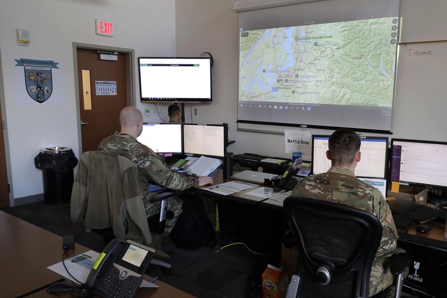 In this Tuesday, March 31, 2020, photo, Washington National Guard soldiers work in front of a map at Camp Murray, Wash., showing locations of area food banks in Washington state. Guard soldiers are expected to deploy later in the week to assist with food bank operations as part of their first mission related to the outbreak of the new coronavirus. (AP Photo/Ted S. Warren)
