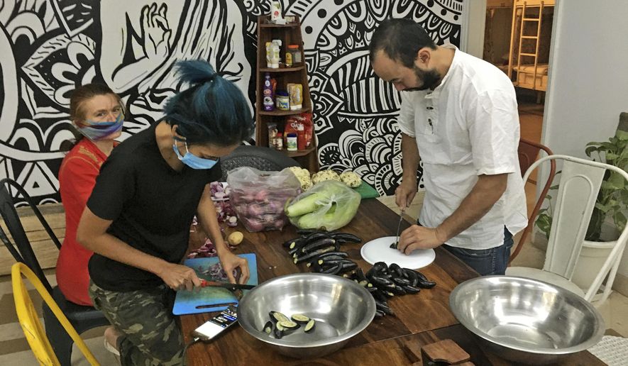 Stranded foreign tourists cut vegetables to make a meal at a hostel in New Delhi, India, Thursday, April 2, 2020. Dozens of tourists from Britain, Canada and Australia are finding themselves stranded in the Indian capital with their vacations abruptly ended by India’s three-week lockdown and stopping of international flights amid new coronavirus. (AP Photo/Shonal Ganguly)
