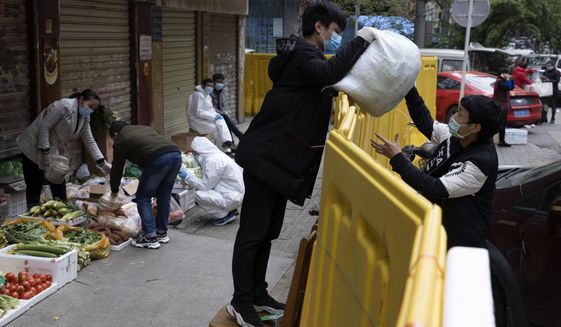 A vendor hands over grocery to another across barriers used to seal off a neighborhood to help curb the spread of the coronavirus in Wuhan, China, Friday, April 3, 2020. Sidewalk vendors wearing face masks and gloves sold pork, tomatoes, carrots and other vegetables to shoppers Friday in the Chinese city where the coronavirus pandemic began as workers prepared for a national memorial this weekend for health workers and others who died in the outbreak. (AP Photo/Ng Han Guan)