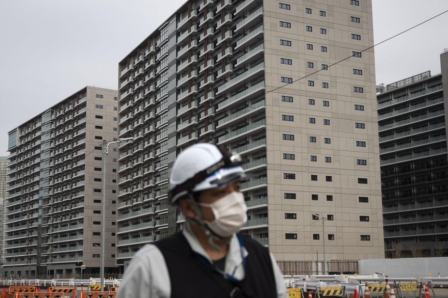 FILE - In this March 23, 2020, file photo, a worker walks through the athletes village for the Tokyo 2020 Olympics, in Tokyo. Tokyo’s governor is considering the possibility of using the unfinished Olympic Athletes Village as a temporary hospital for coronavirus infected patients. The massive village on Tokyo Bay could house up to 18,000 people during the Olympics. (AP Photo/Jae C. Hong, File)