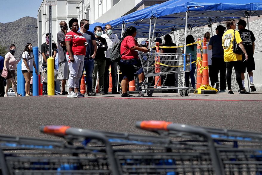 Some people wearing face masks wait in line to shop Saturday, April 4, 2020, in Tempe, Ariz. Honeywell announced that it is adding manufacturing capabilities in Phoenix to produce N95 face masks in support of the government's response to the novel coronavirus The company's Phoenix expansion will allow Honeywell to produce more than 20 million N95 disposable masks monthly to combat COVID-19 in the U.S. The new coronavirus causes mild or moderate symptoms for most people, but for some, especially older adults and people with existing health problems, it can cause more severe illness or death. (AP Photo/Matt York)