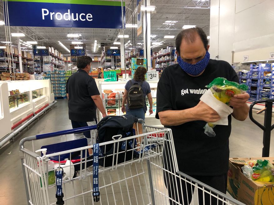 In this Tuesday, March 31, 2020 photo, comedian Frank De Lima wears a masks and maintains social distancing while wiping a package of bananas at a Sam's Club store in Honolulu. (AP Photo/Jennifer Sinco Kelleher)
