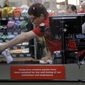In this March 26, 2020, file photo, Garrett Ward sprays disinfectant on a conveyor belt between checking out shoppers behind a plexiglass panel at a Hy-Vee grocery store in Overland Park, Kan. From South Africa to Italy to the U.S., grocery workers — many in low-wage jobs — are manning the front lines amid worldwide lockdowns, their work deemed essential to keep food and critical goods flowing. (AP Photo/Charlie Riedel, File)