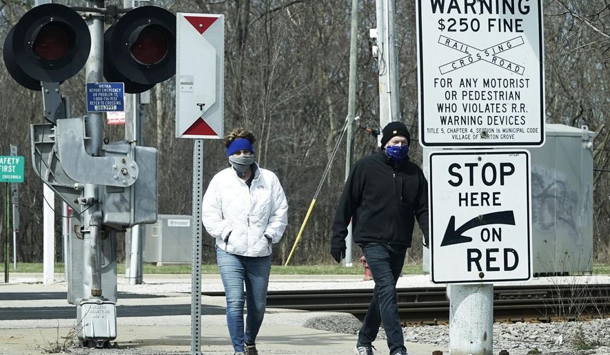 People cover their faces with cloths as they walk on the sidewalk in Morton Grove, Ill., Sunday, April 5, 2020. The new coronavirus causes mild or moderate symptoms for most people, but for some, especially older adults and people with existing health problems, it can cause more severe illness or death. (AP Photo/Nam Y. Huh)