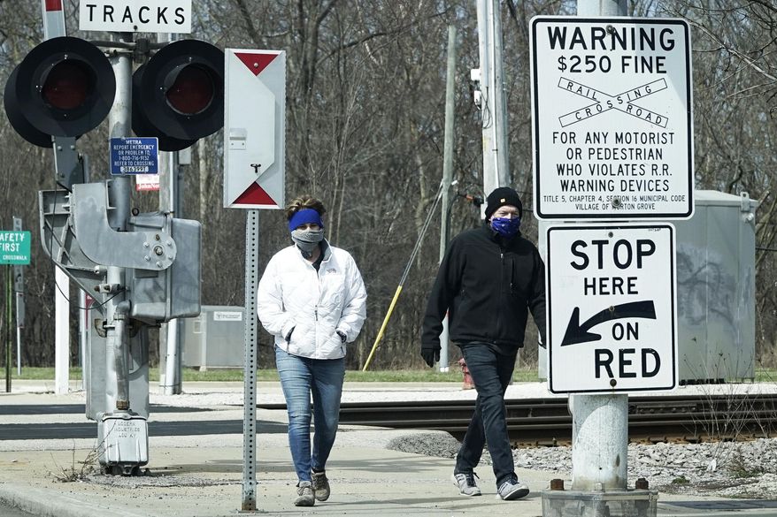 People cover their faces with cloths as they walk on the sidewalk in Morton Grove, Ill., Sunday, April 5, 2020. The new coronavirus causes mild or moderate symptoms for most people, but for some, especially older adults and people with existing health problems, it can cause more severe illness or death. (AP Photo/Nam Y. Huh)