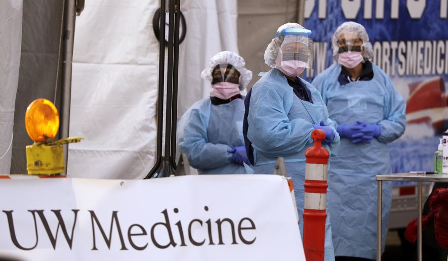 FILE - In this March 17, 2020, file photo, medical personnel wait for a driver to pull up at a drive-thru COVID-19 testing station for University of Washington Medicine patients in Seattle. Experts and health officials who are trying to plan a response to the coronavirus outbreak are missing a critical piece of information – the number of health care workers who have tested positive for the disease. (AP Photo/Elaine Thompson, File)