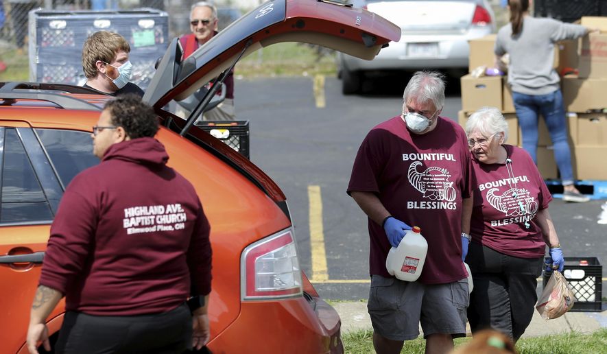Church members Brian Helton and Donna Covert help load food during a drive-thru food distribution service Saturday, April 4, 2020, in front of Highland Avenue Baptist Church in Elmwood Place, Ohio. At least 800 vehicles passed through, each receiving a pre-packed 40-pound emergency food box with staples like peanut butter, spaghetti, canned fruits, vegetables, oatmeal, and chili, and two gallons of milk, a frozen chicken,18 eggs and produce from the Freestore Foodbank of Cincinnati, according to Jessie Fossenkemper, the community partnership manager. (Kareem Elgazzar/The Cincinnati Enquirer via AP)
